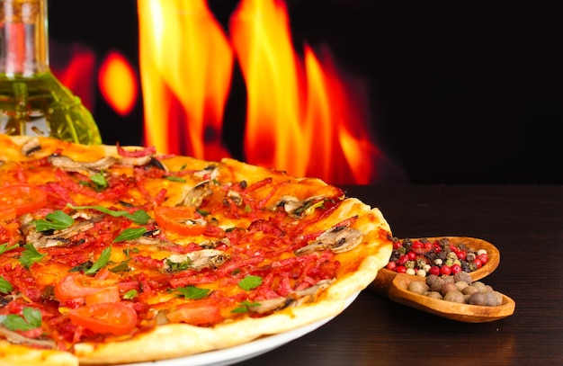 Delicious pizza with vegetables and salami on wooden table on flame background