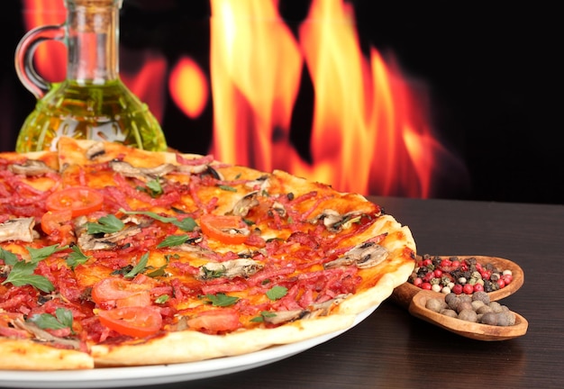 炎の背景に木製のテーブルに野菜とサラミのおいしいピザ