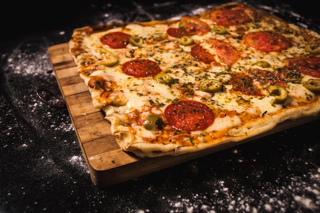 Delicious pizza on a wooden board, on a black surface