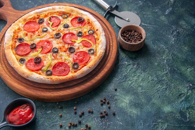 Delicious pizza on wooden cutting board and pepper ketchup on isolated dark surface in close up view