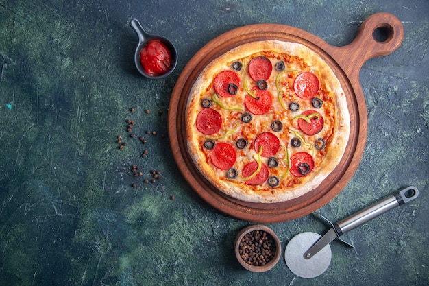 Delicious pizza on wooden cutting board and pepper ketchup on the left side on isolated dark surface