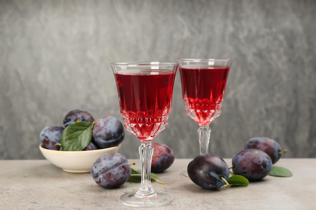 Delicious plum liquor and ripe fruits on table against grey background Homemade strong alcoholic beverage