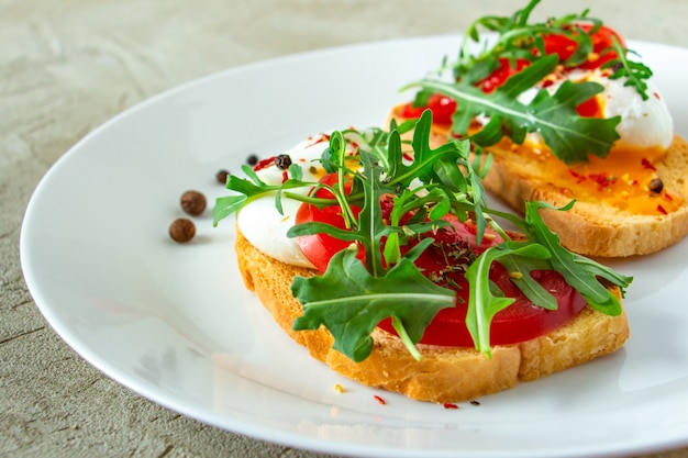 delicious poached egg on two slices of white bread with arugula mozzarella and tomatoes