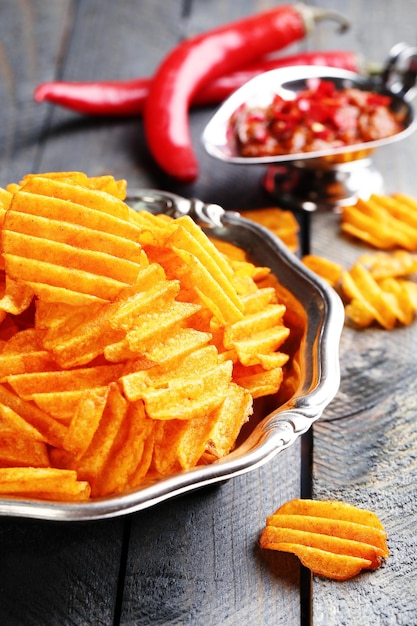 Delicious potato chips on plate on wooden table closeup