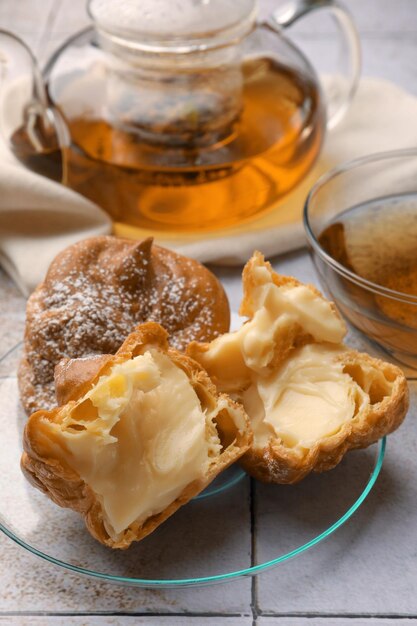 Delicious profiteroles filled with cream and tea on white tiled table closeup