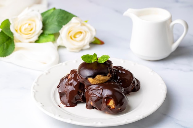 Delicious profiteroles with chocolate and white plate. Selective focus image on light background.