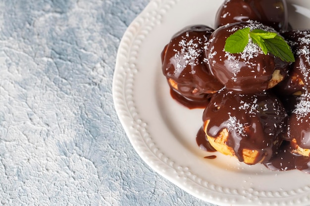 Delicious profiteroles with chocolate and white plate. Selective focus image on light background.