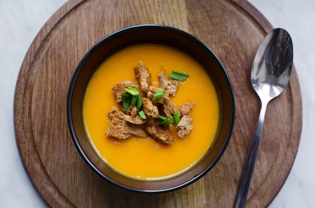 Delicious pumpkin soup in black plate with crackers