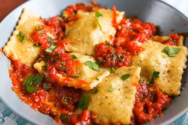 Deliziosi ravioli con salsa di pomodoro in un piatto su fondo di legno