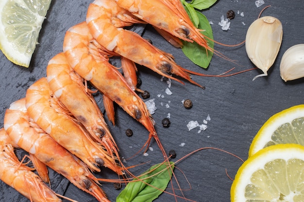 Delicious red boiled shrimps with lemon garlic salt and pepper with herbs on dark board