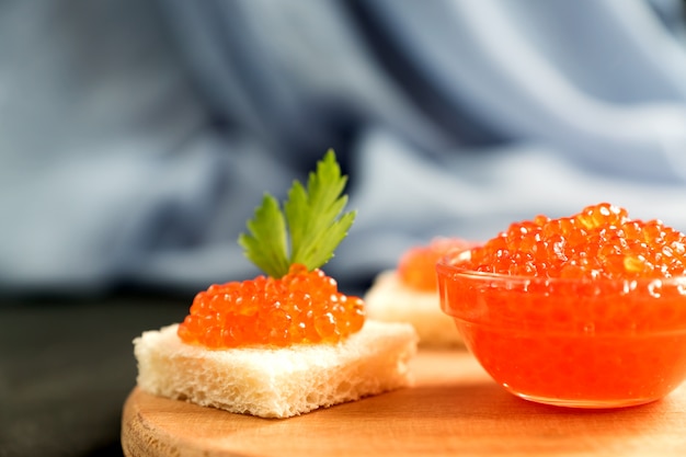 Delicious red caviar on wheat bread served with parseley on wooden desk.
