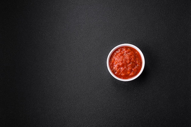 Foto deliziosa salsa napoletana rossa con cipolle, sale, spezie ed erbe aromatiche in una ciotola bianca su fondo di cemento scuro