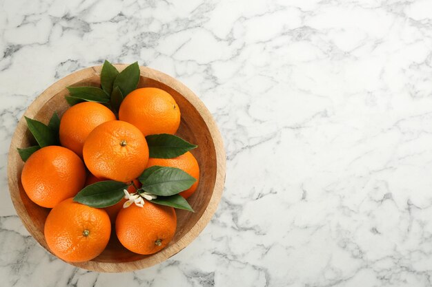 Delicious ripe oranges in bowl on white marble table top view space for text