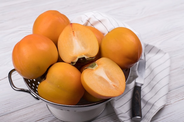 Delicious ripe persimmon fruit on white wooden table