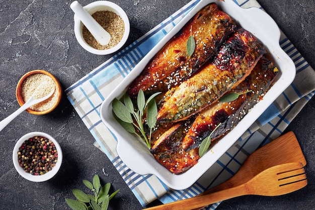 Delicious roasted wedges of mackerel in a baking dish on a concrete table with spices at the surface, view from above, flat lay, close-up