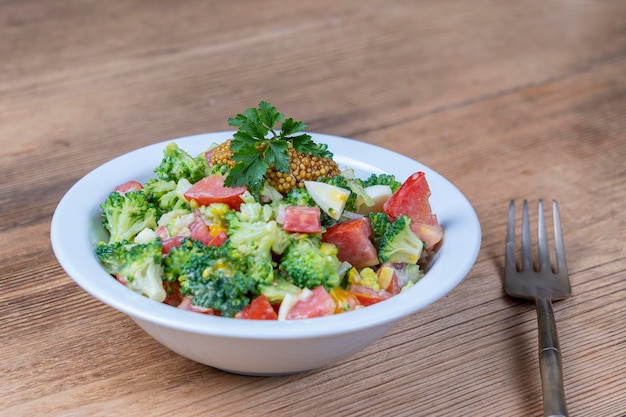 Delicious salad with broccoli tomato onion and boiled egg with cream sauce in plate on wooden background Healthy food