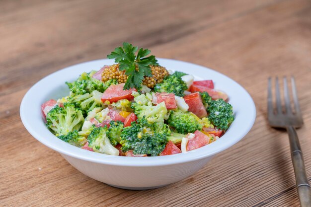 Delicious salad with broccoli tomato onion and boiled egg with cream sauce in plate on wooden background Healthy food