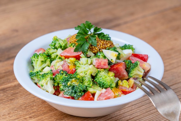 Delicious salad with broccoli tomato onion and boiled egg with cream sauce in plate on wooden background Healthy food