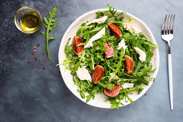 Delicious salad with figs arugula and goat cheese on white plate top view copy space