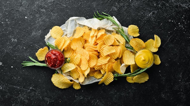 Delicious salty potato chips Beer snacks on a black stone background Top view Free space for your text