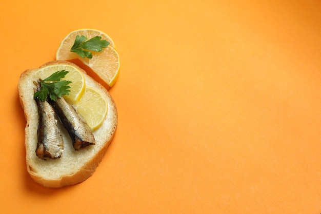 Delicious sandwich with sprats on orange background