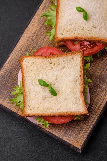 Delicious sandwich with toast ham tomatoes cheese and lettuce with salt spices and herbs on a dark concrete background