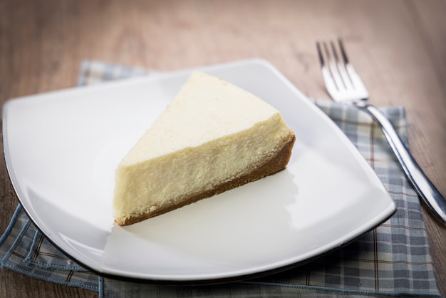 delicious slice of plain cheesecake on a white plate on a wooden table