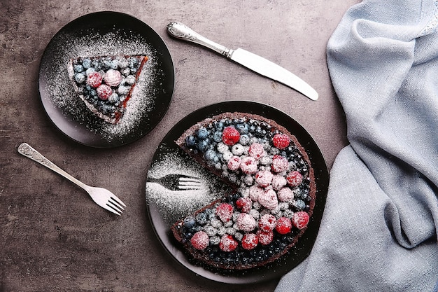 Delicious sliced chocolate tart with berries on black plate