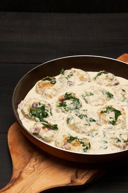 Delicious small meatballs with spinach in a creamy sauce in the frying pan