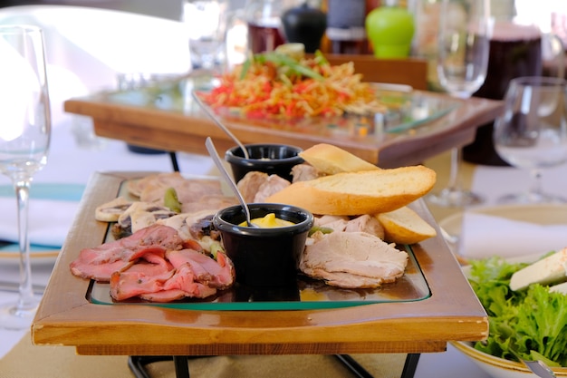 Foto deliziosa pancetta affumicata tagliata su un vassoio di legno su un tavolo per banchetti in un ristorante di lusso