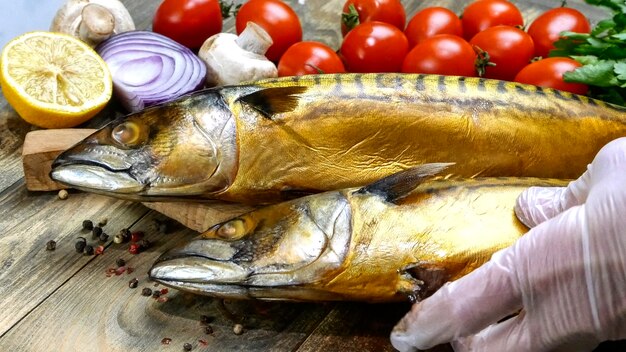 Delizioso sgombro di pesce affumicato su un tavolo di legno accanto a pomodorini, cipolla, funghi e prezzemolo