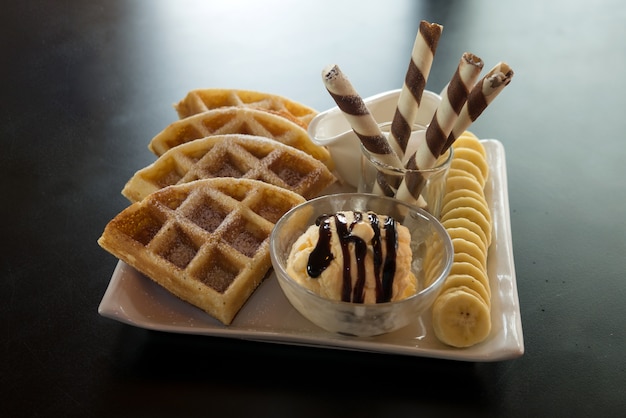 Photo delicious snack baked waffles served with banana and honey syrup topped with chocolate