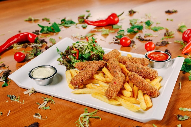 Delicious snack plate, french fries, onion rings, spring rolls\
or sausages on the table