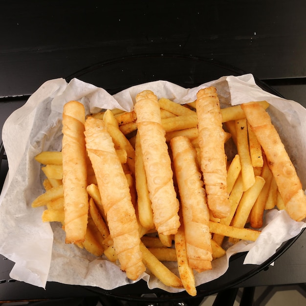 Delicious snack plate, french fries, onion rings, spring rolls\
or sausages on the table