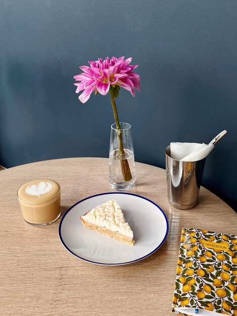 Delicious snack with coffee and dessert on a plate. Fresh pink flower and a notebook for writing