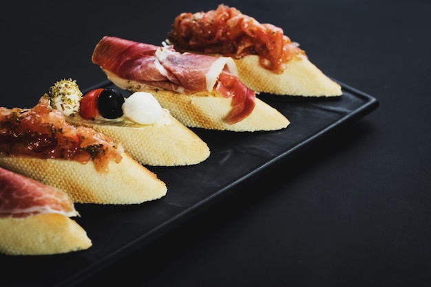 Deliziosi snack con prosciutto a forma di barchetta su sfondo nero. copia spazio