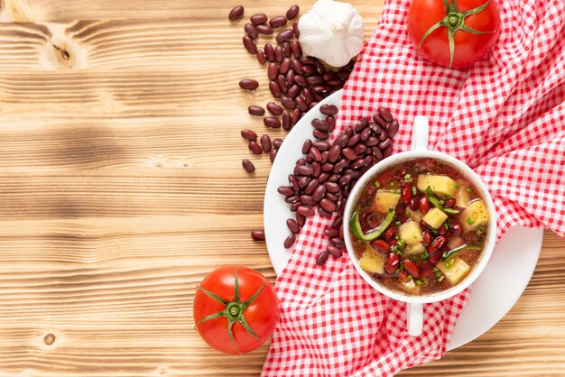 Delicious soup of fresh red beans with the addition of meat, potatoes and herbs on a wooden background.