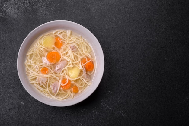 Delicious soup with noodles chicken and carrots with spices and herbs on a dark concrete background