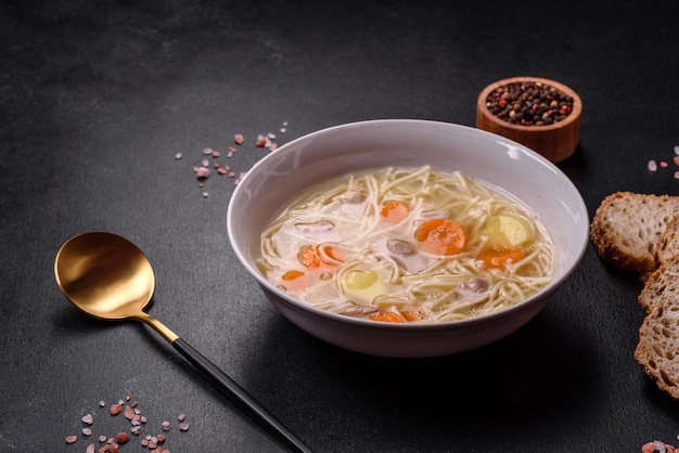 Delicious soup with noodles chicken and carrots with spices and herbs on a dark concrete background