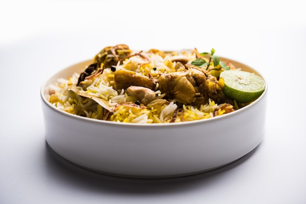 不機嫌そうな背景の上にボウルに入れられたおいしいスパイシーなチキンビリヤニ、それは人気のあるインド料理とパキスタン料理です