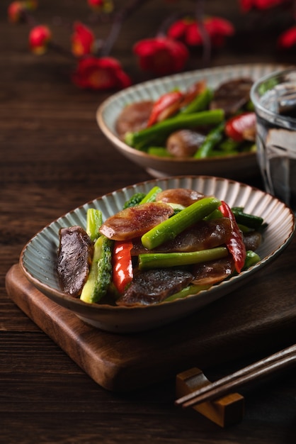 Delicious spicy homemade stir-fried Chinese smoked sausage with asparagus on dark wooden table for meal.