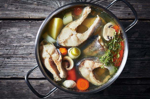 Вкусный острый рыбный суп из форели с овощами и грибами в горшочке на деревянном деревенском столе, горизонтальный вид сверху, крупный план