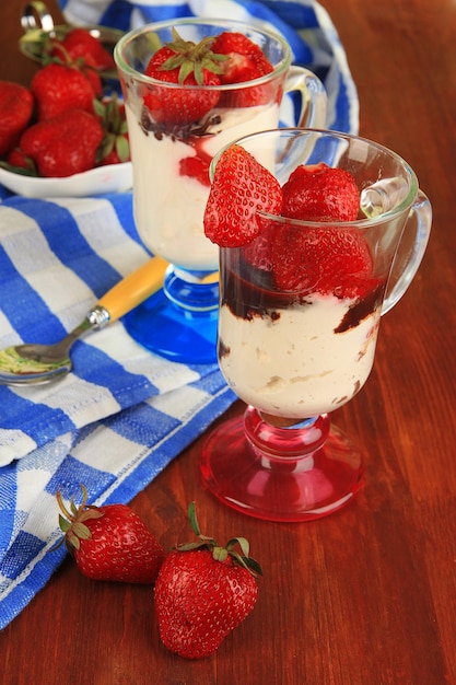 Delicious strawberry desserts in glass vase on wooden table closeup