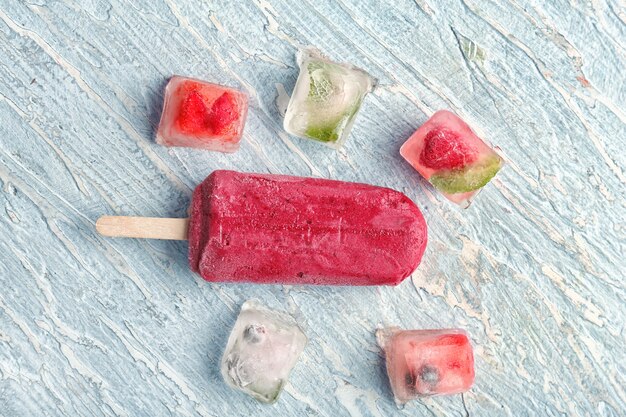 Deliziosi ghiaccioli alla fragola e cubetti di ghiaccio con frutti di bosco sulla superficie in legno