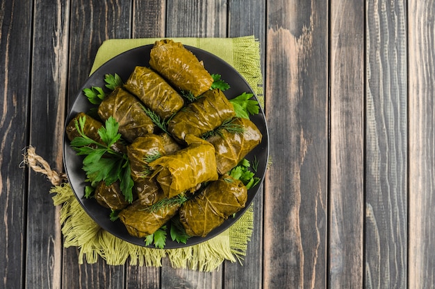 Delicious stuffed grape leaves on a black plate with fresh cilantro and dill