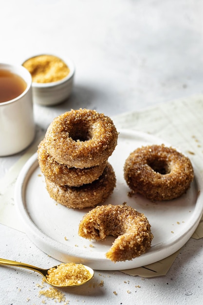 Delicious sugar coated donuts on a plate on white textured background with tea and sugar