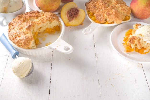 Delicious Summer Peach Cobbler, Homemade sweet summer pie with peaches and vanilla ice cream on white wooden background copy space