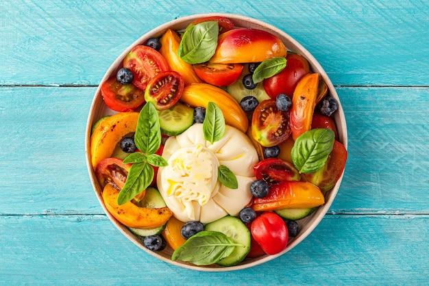 Delicious summer salad with burrata cheese grilled peaches tomatoes blueberries cucumber olive oil and basil