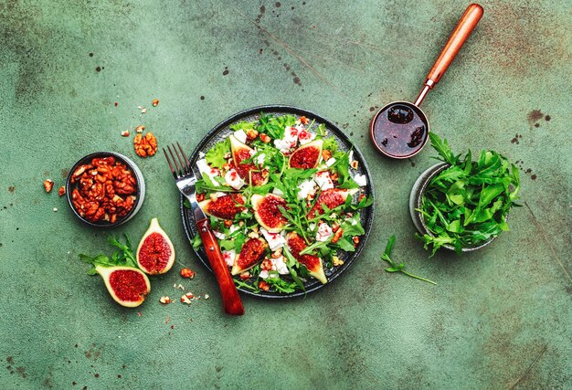 Delicious summer salad with figs feta cheese walnuts arugula and sweet jam dressing on rusty green table background top view negative space