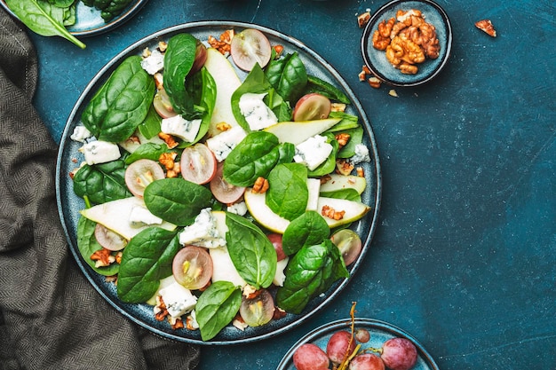 Delicious summer salad with pear grapes roquefort cheese spinach walnuts on blue table background top view negative space